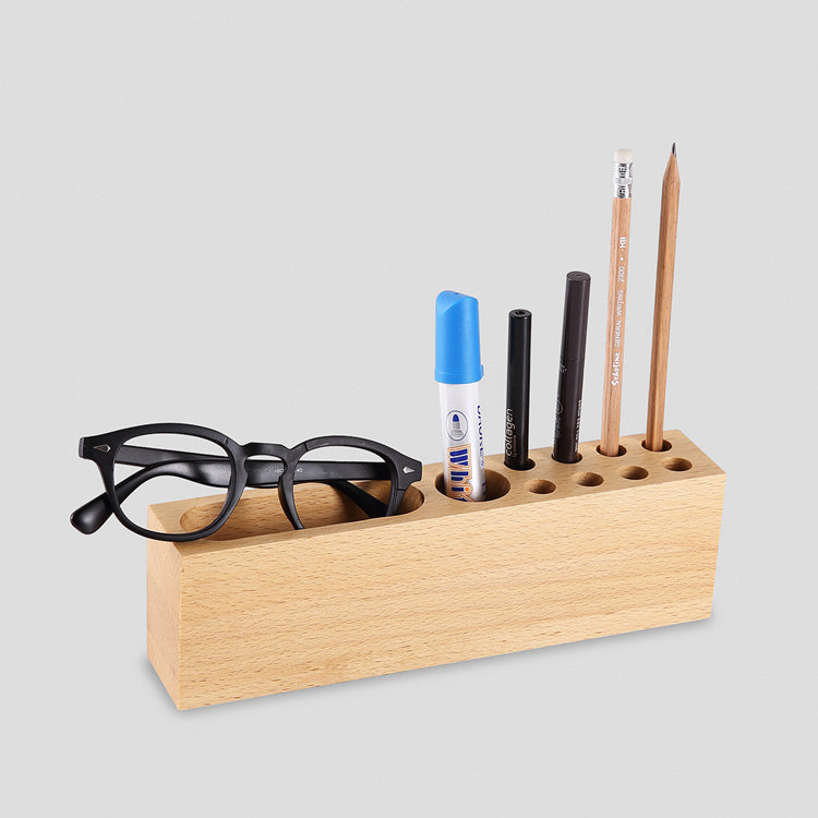 Wooden pen holder with glasses, markers, and pencils on a light gray background
